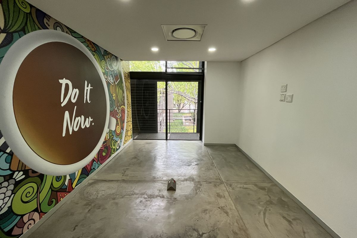 A modern, empty office space featuring polished concrete floors, recessed lighting, integrated air conditioning, and a large sliding glass door leading to a balcony.