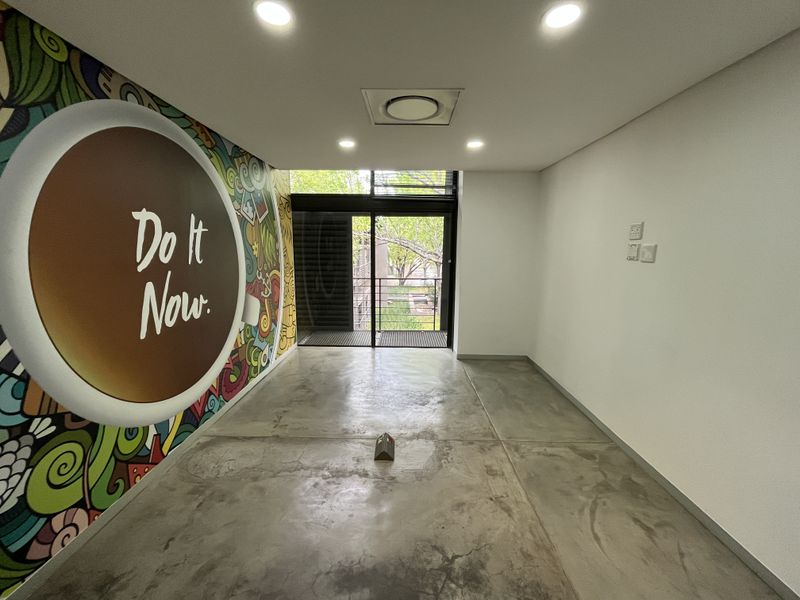 A modern, empty office space featuring polished concrete floors, recessed lighting, integrated air conditioning, and a large sliding glass door leading to a balcony.