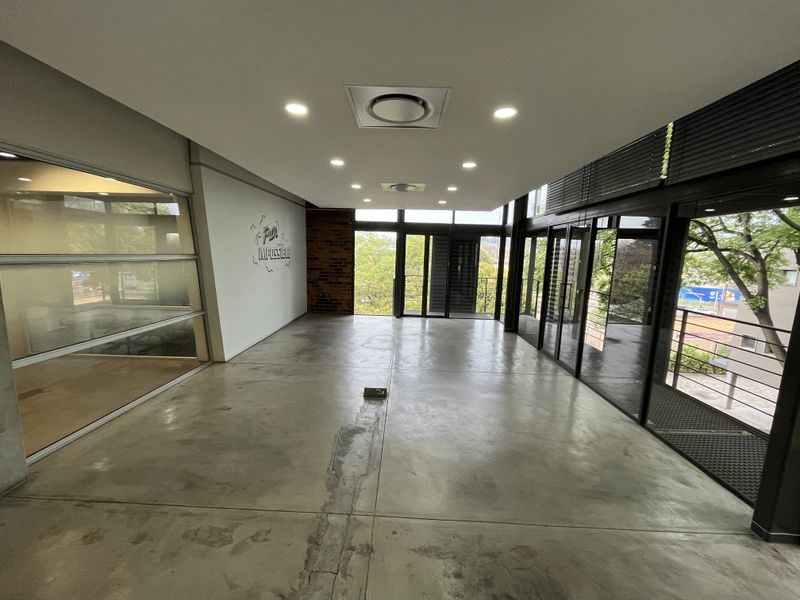 Spacious open-plan office area featuring polished concrete floors, exposed brick accents, and extensive floor-to-ceiling glass windows providing ample natural light.