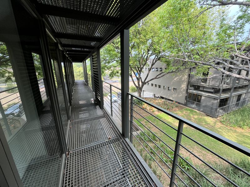 A modern industrial-style metal balcony walkway featuring mesh flooring, louvered overhead shading, and a metal balustrade overlooking the office park grounds.