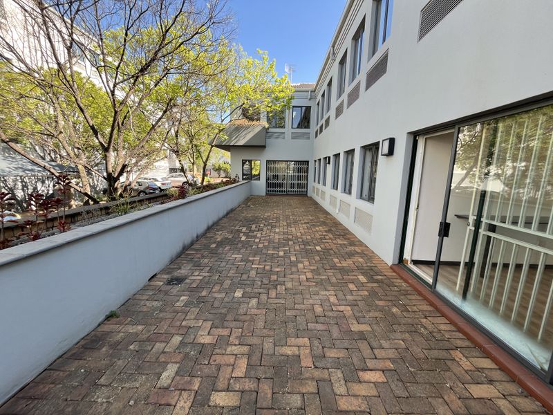 A paved outdoor patio area adjacent to the office building, featuring a retaining wall and direct access through sliding glass doors.