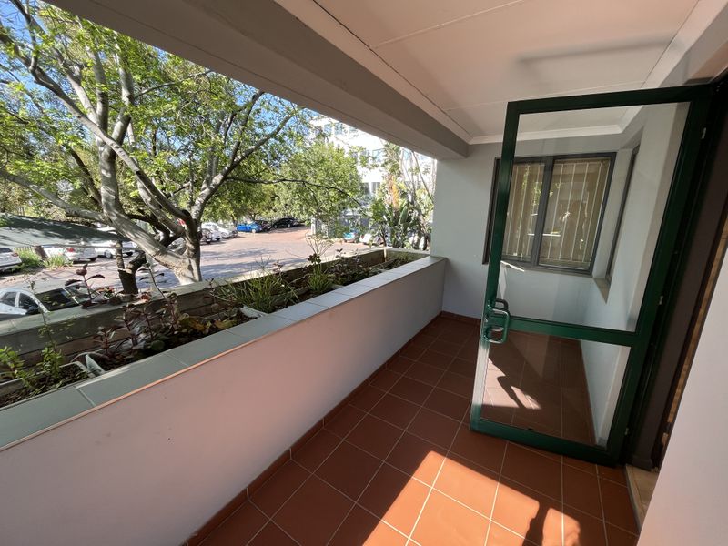 A clean, tiled balcony featuring a built-in planter box and an aluminium-framed glass door, offering a pleasant outdoor space.