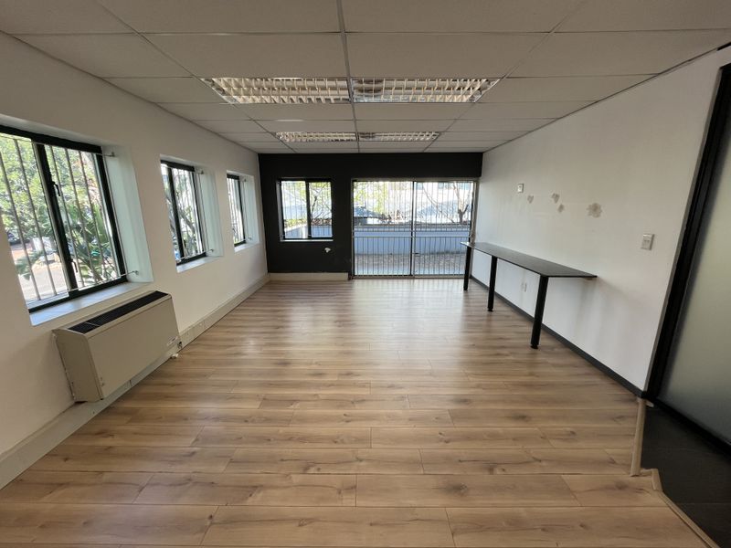 An empty office space featuring laminate flooring, a suspended ceiling with recessed lighting, a wall-mounted HVAC unit, and a built-in desk.