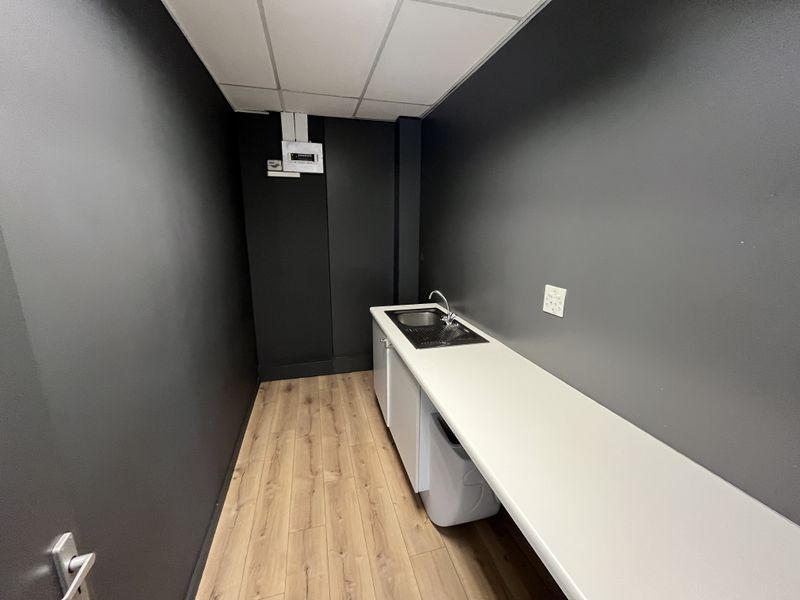 A clean utility space featuring a sink, built-in cabinetry, countertop, and modern laminate flooring, suitable for office storage or a kitchenette area.