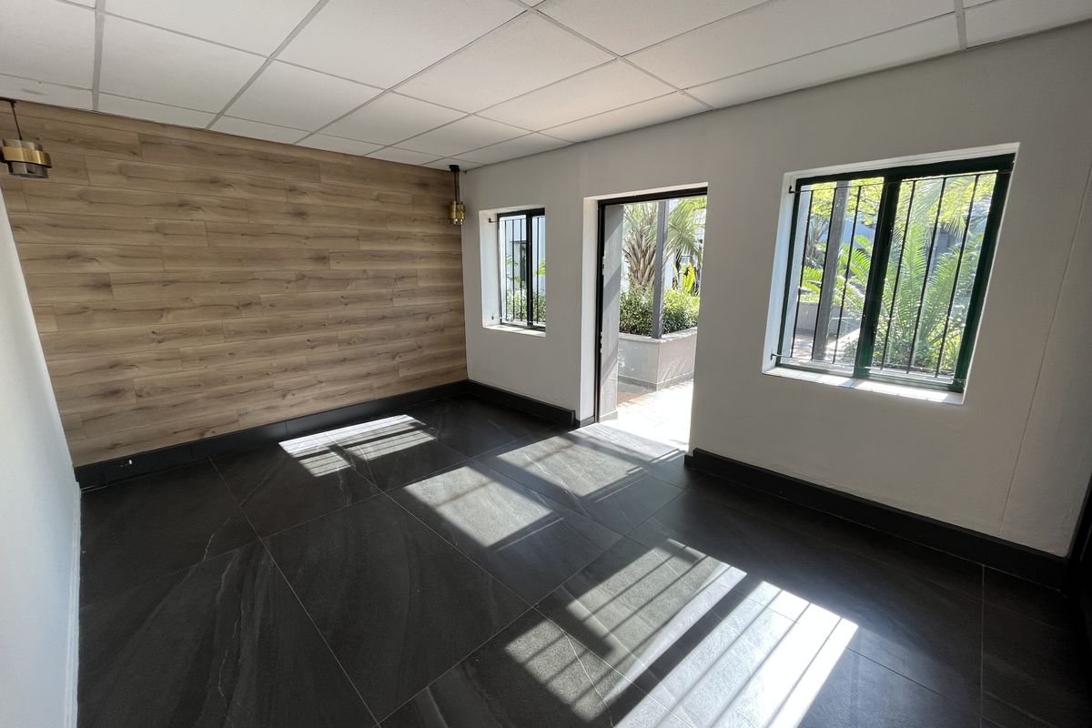 A bright, modern office space featuring wood-look accent wall paneling, large format dark floor tiles, and direct access to an outdoor area.