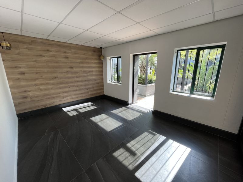 A bright, modern office space featuring wood-look accent wall paneling, large format dark floor tiles, and direct access to an outdoor area.