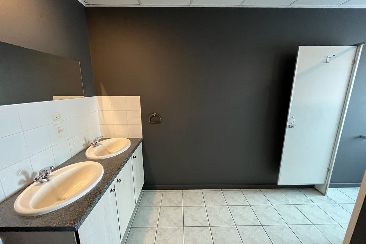 A functional office bathroom featuring a double vanity with drop-in sinks, tiled flooring, and a neutral dark wall finish.