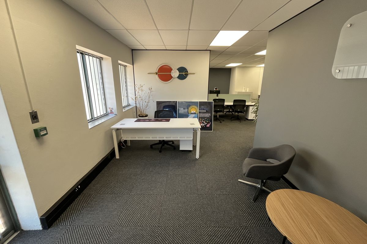 A professional office space featuring a suspended ceiling, recessed lighting, security bars on windows, and patterned carpet flooring.