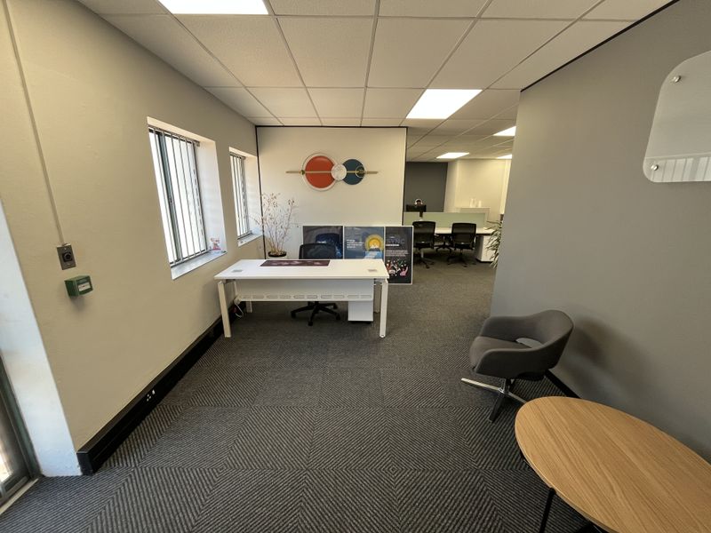 A professional office space featuring a suspended ceiling, recessed lighting, security bars on windows, and patterned carpet flooring.