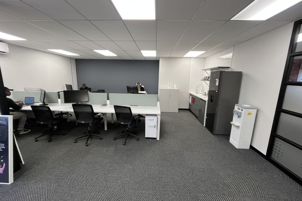 A modern, well-maintained office space featuring a partitioned workstation area, integrated kitchenette with sink, and professional suspended ceiling lighting.