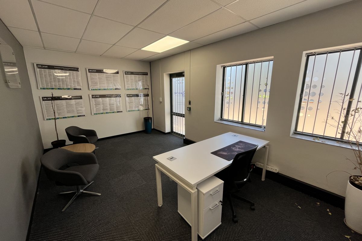 A professional office space featuring a suspended ceiling, recessed lighting, carpeted flooring, and windows equipped with security bars and privacy film.