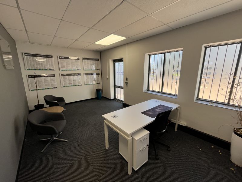 A professional office space featuring a suspended ceiling, recessed lighting, carpeted flooring, and windows equipped with security bars and privacy film.