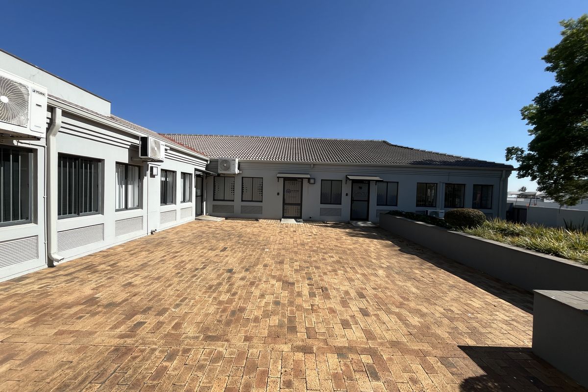 A well-maintained office exterior featuring a spacious brick-paved courtyard, secure building access, and integrated air conditioning units.
