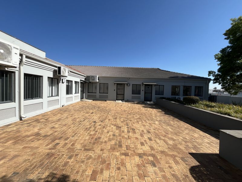 A well-maintained office exterior featuring a spacious brick-paved courtyard, secure building access, and integrated air conditioning units.