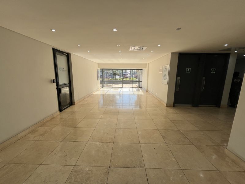 A bright and spacious office entrance lobby featuring polished tiled flooring, recessed ceiling lighting, and glass-paneled access doors.