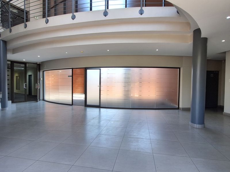 Spacious modern office lobby featuring a curved glass partition, tiled flooring, and a mezzanine level with a metal staircase.