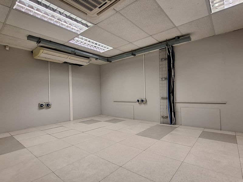 An empty office space featuring a suspended ceiling, wall-mounted air conditioning, and raised access flooring with exposed cable management systems.