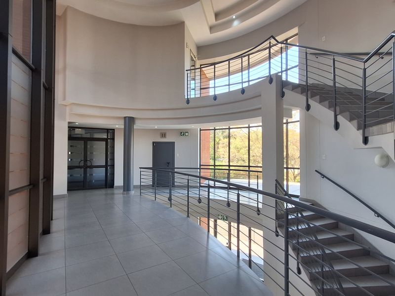 Spacious modern office building entrance featuring a grand curved staircase, tiled flooring, and expansive glass windows providing ample natural light.
