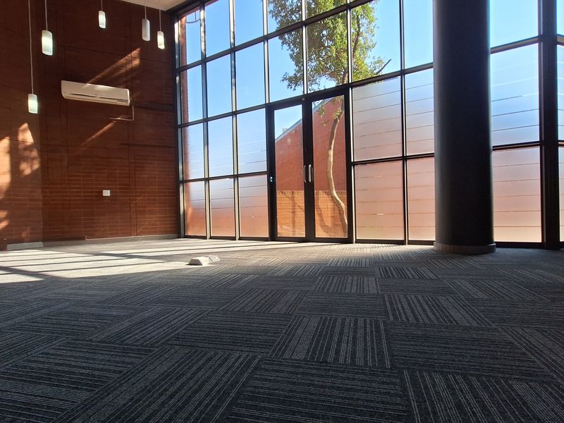 Spacious, modern office area featuring floor-to-ceiling windows, exposed brick walls, and high-quality carpet tiles, offering a bright and professional workspace.