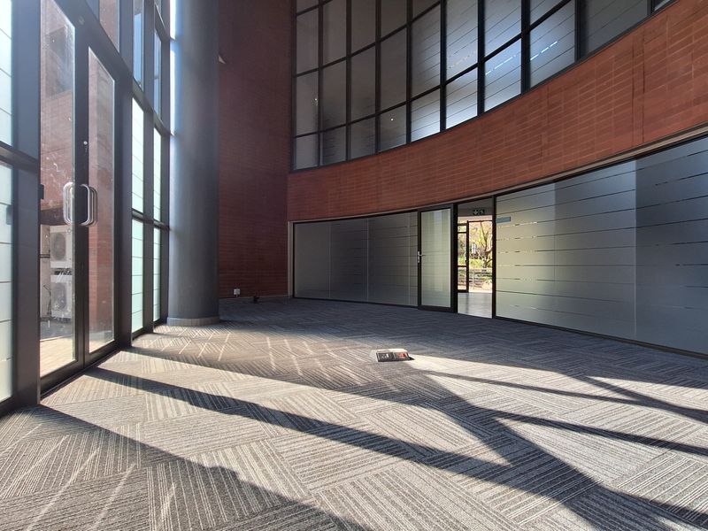 Spacious, modern office area featuring floor-to-ceiling windows, glass partitions, and exposed brick walls, offering a bright and professional workspace environment.