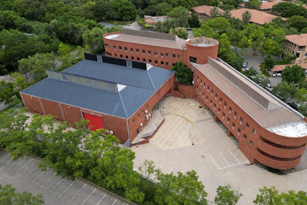 Aerial view of a multi-story office complex featuring brick architecture, a large warehouse-style building, and an expansive paved parking lot.