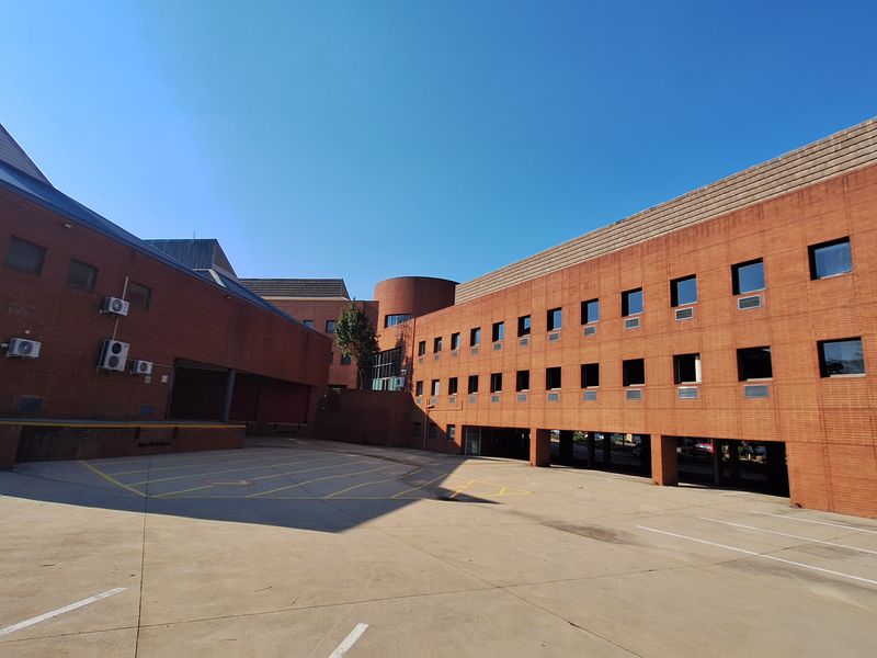 A wide-angle view of the industrial property's rear exterior, featuring a large concrete yard, brick facade, and integrated loading bay area.
