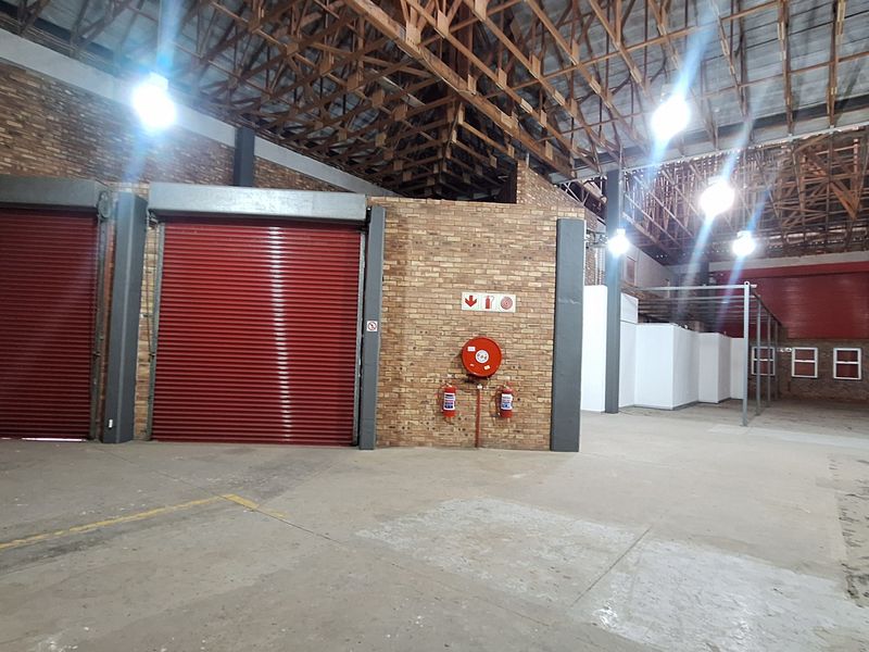 Spacious industrial warehouse unit featuring exposed brick walls, high timber roof trusses, concrete flooring, and multiple roller shutter doors for efficient access.