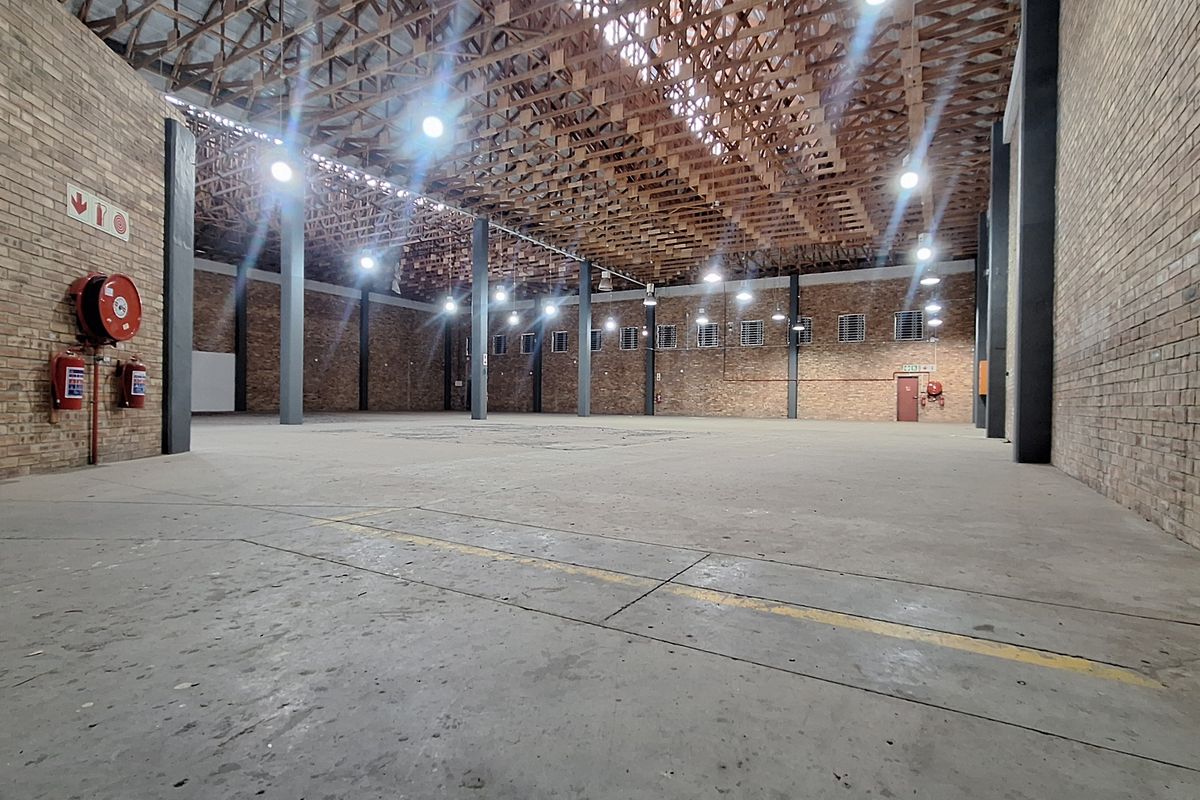 Spacious industrial warehouse featuring exposed brick walls, high timber roof trusses, concrete flooring, and steel support columns, suitable for storage or manufacturing.