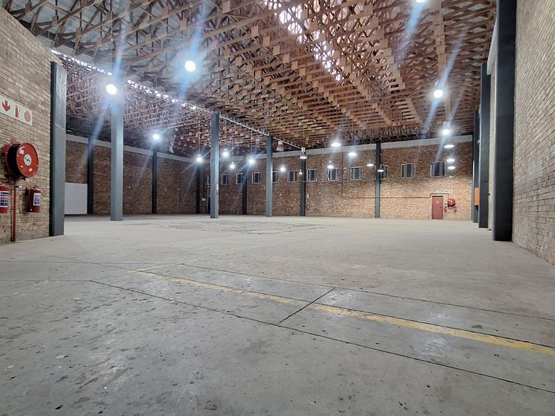 Spacious industrial warehouse featuring exposed brick walls, high timber roof trusses, concrete flooring, and steel support columns, suitable for storage or manufacturing.