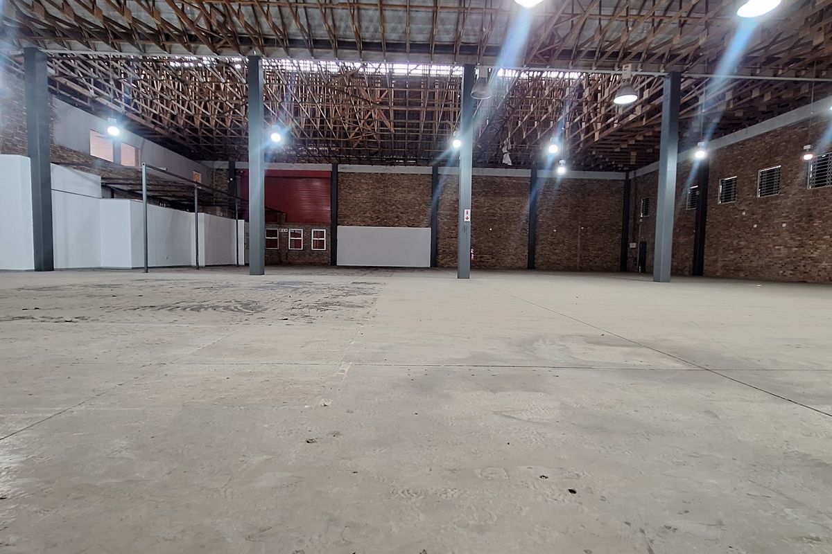 Spacious industrial warehouse featuring exposed timber roof trusses, steel support columns, brick walls, and durable concrete flooring, suitable for various commercial or storage uses.