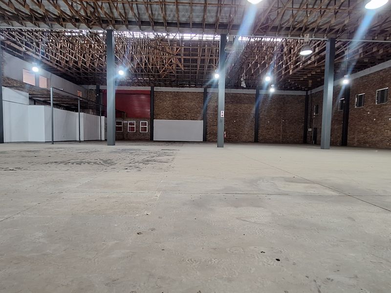 Spacious industrial warehouse featuring exposed timber roof trusses, steel support columns, brick walls, and durable concrete flooring, suitable for various commercial or storage uses.