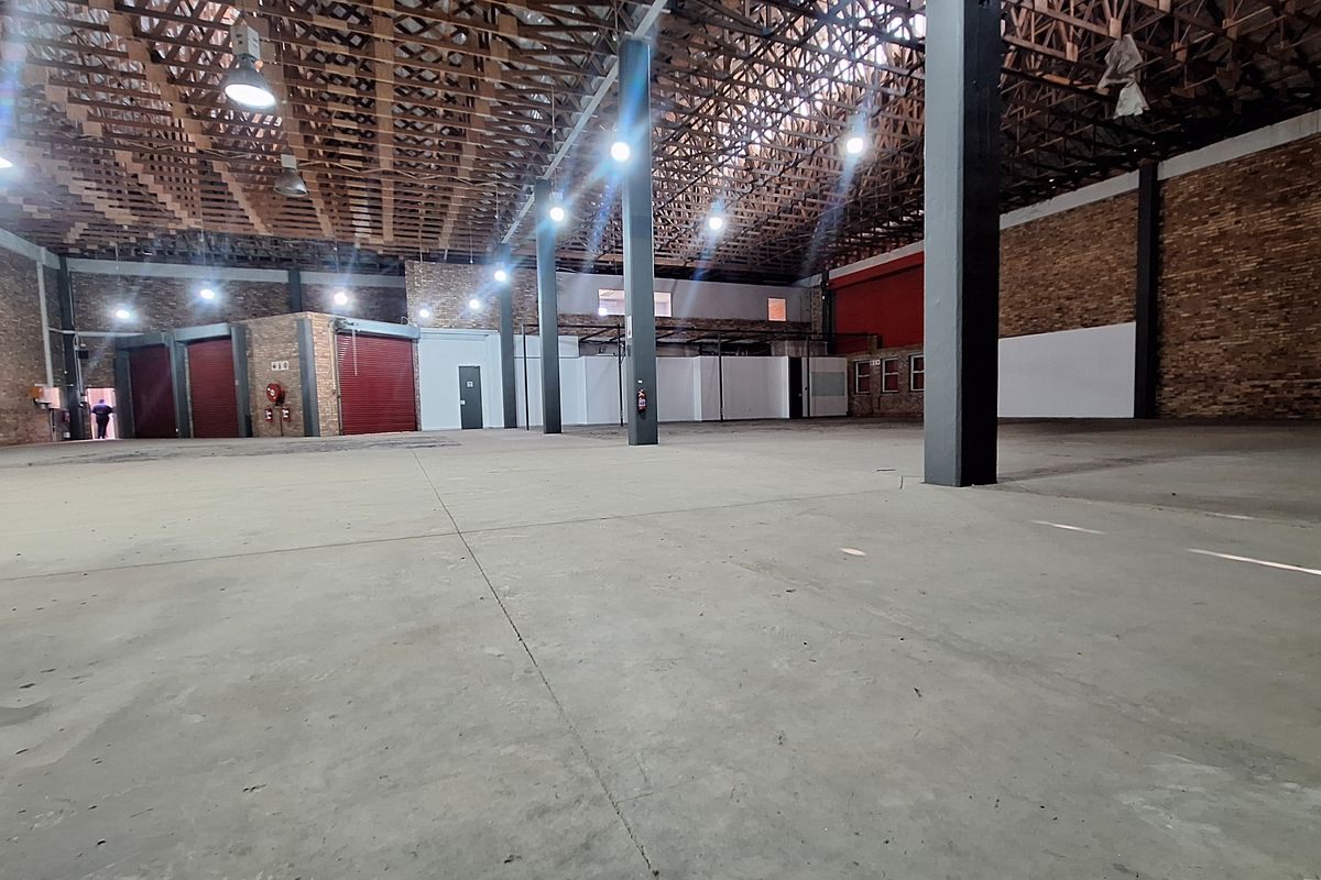 Spacious industrial warehouse featuring exposed timber roof trusses, concrete flooring, steel support columns, and multiple roller shutter doors for efficient access.