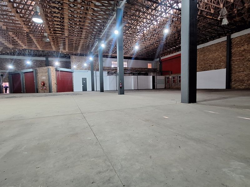 Spacious industrial warehouse featuring exposed timber roof trusses, concrete flooring, steel support columns, and multiple roller shutter doors for efficient access.