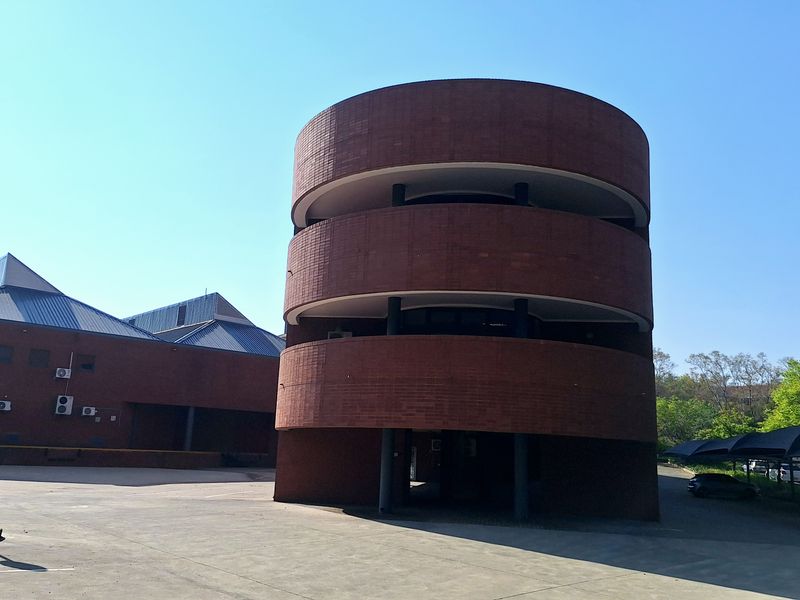 Exterior view of a distinctive circular brick industrial building featuring multi-level design, paved driveway, and adjacent covered parking facilities.