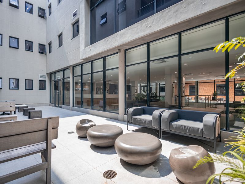 A modern, paved outdoor courtyard area featuring large glass office facades, concrete structural elements, and integrated drainage, providing a clean and professional exterior space.