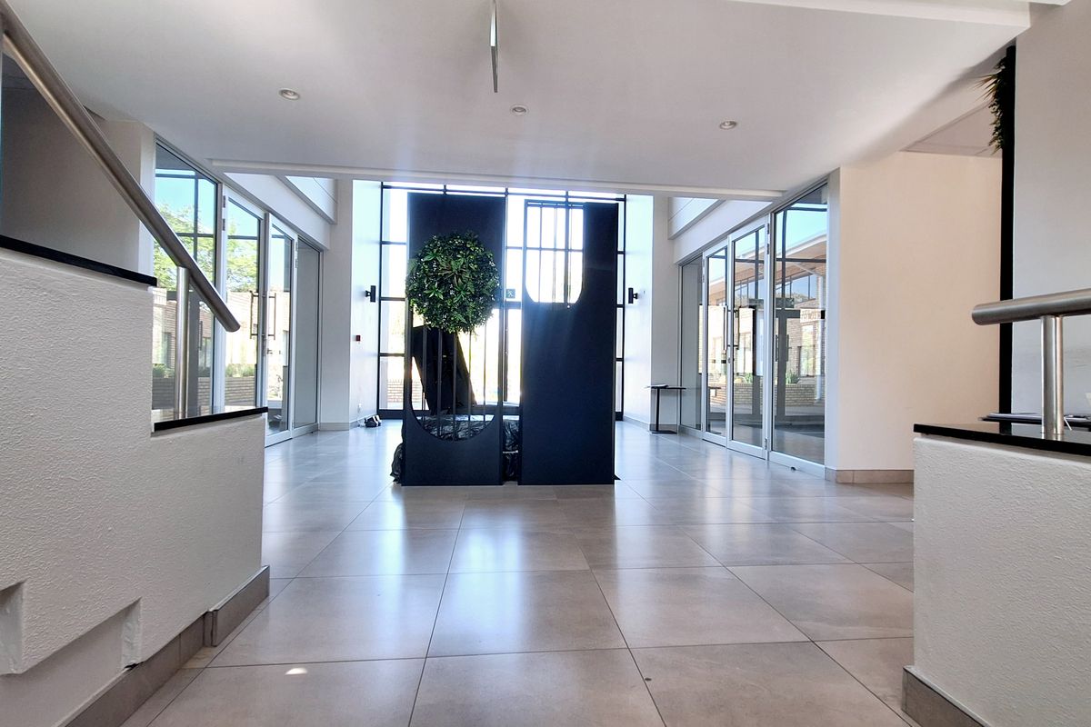 Spacious modern office entrance lobby featuring large glass panels, tiled flooring, and clean architectural lines, providing a bright and professional welcome area.