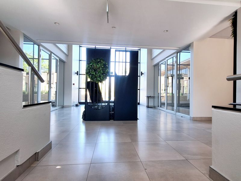 Spacious modern office entrance lobby featuring large glass panels, tiled flooring, and clean architectural lines, providing a bright and professional welcome area.