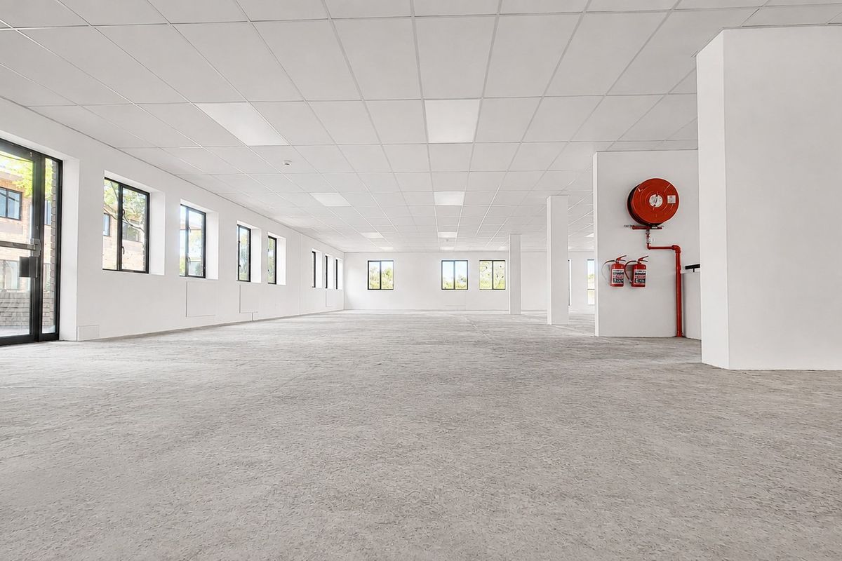 A spacious, open-plan office area featuring a suspended ceiling, recessed lighting, and essential fire safety equipment, offering a clean and versatile workspace.