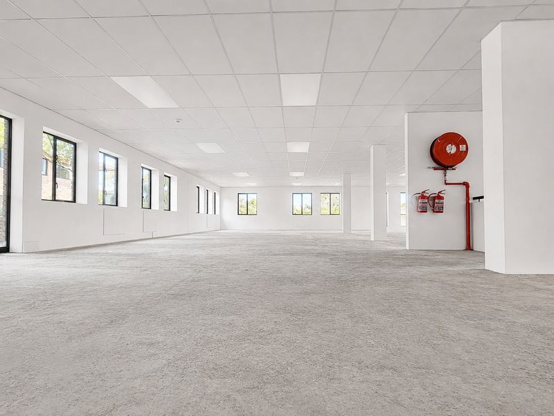 A spacious, open-plan office area featuring a suspended ceiling, recessed lighting, and essential fire safety equipment, offering a clean and versatile workspace.