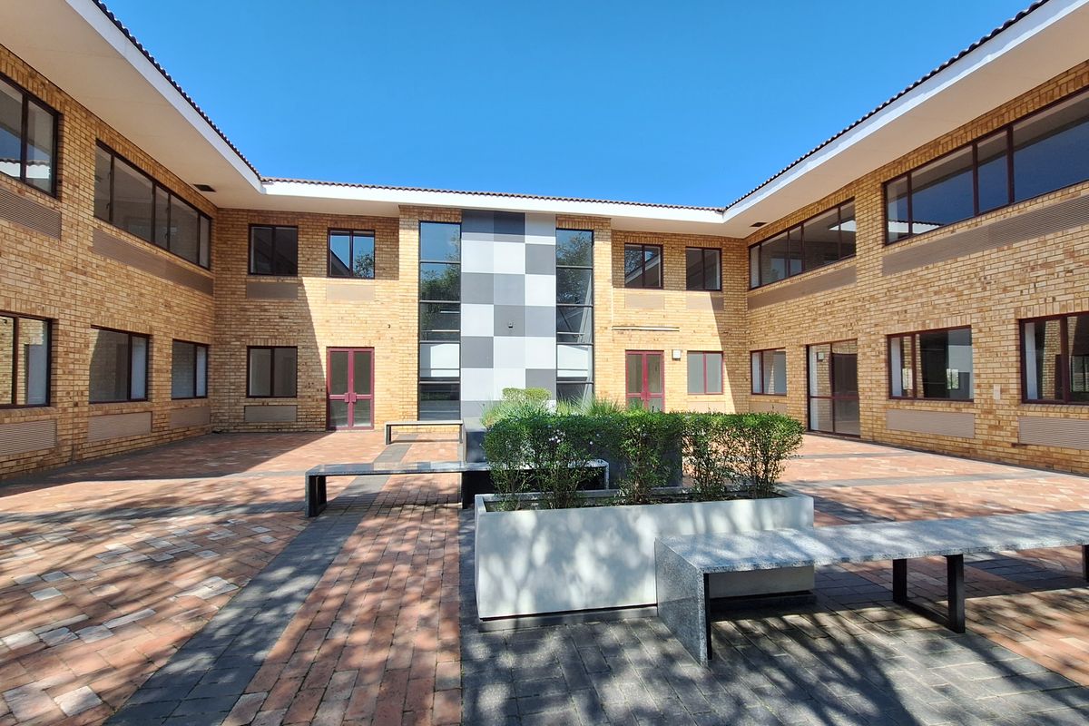A well-maintained office courtyard featuring brick architecture, paved walkways, built-in stone seating, and integrated planter boxes within a secure building complex.