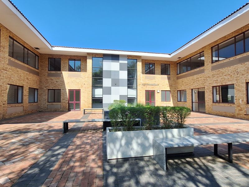A well-maintained office courtyard featuring brick architecture, paved walkways, built-in stone seating, and integrated planter boxes within a secure building complex.