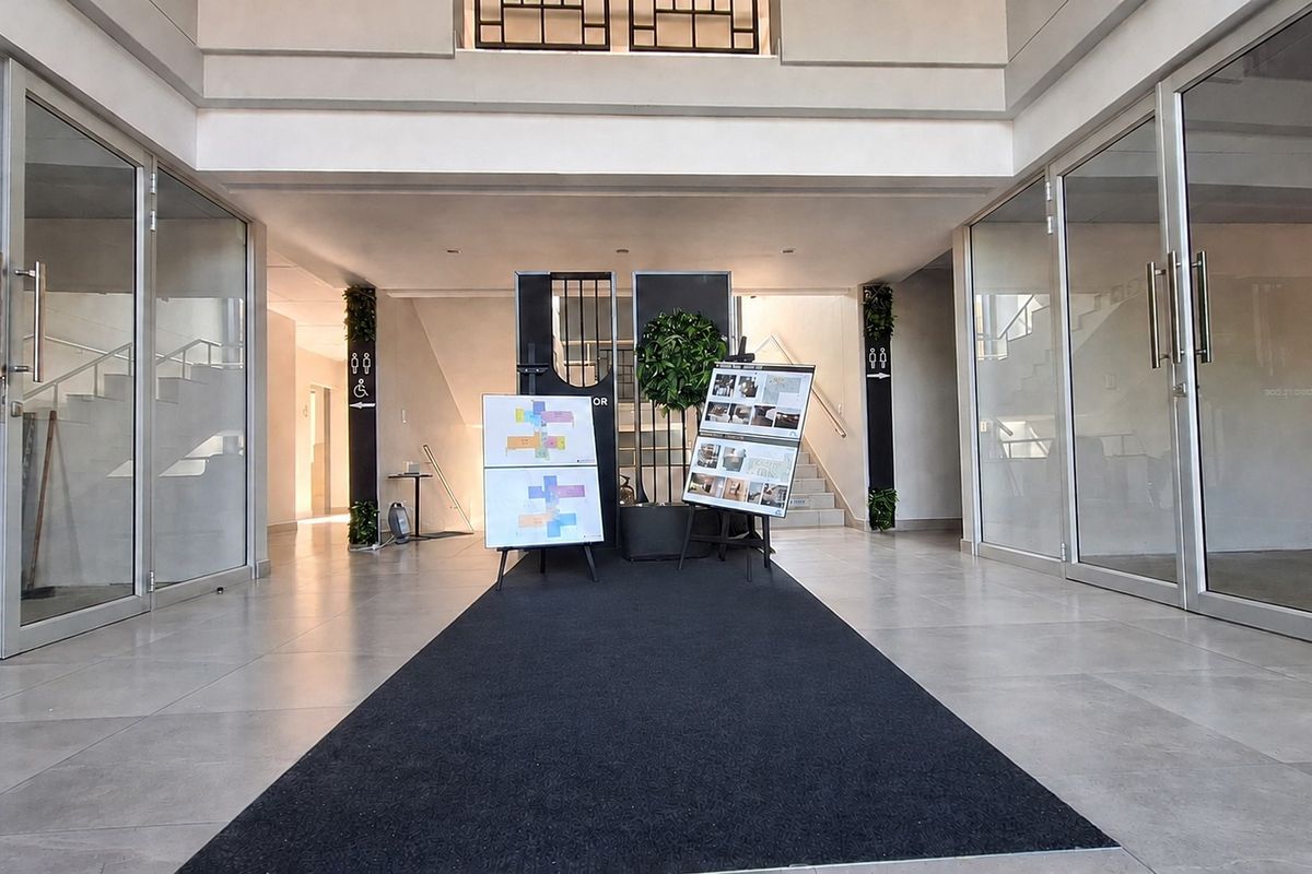 A spacious and modern office building entrance lobby featuring glass-partitioned office spaces, neutral tiled flooring, and a central staircase.