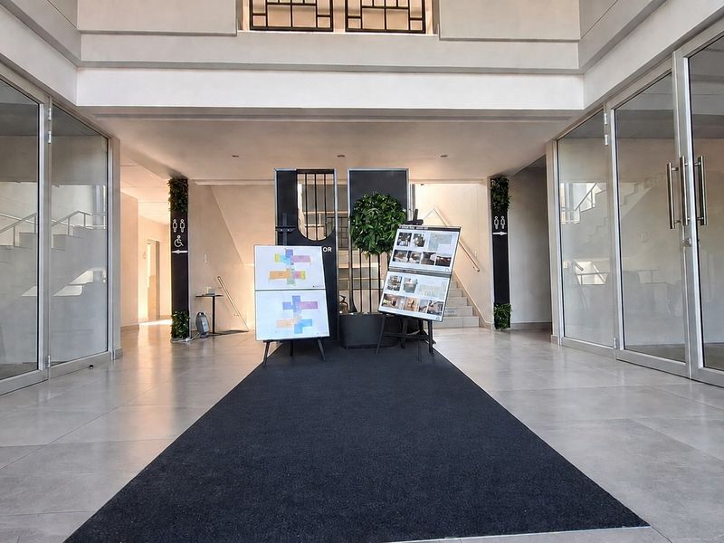 A spacious and modern office building entrance lobby featuring glass-partitioned office spaces, neutral tiled flooring, and a central staircase.