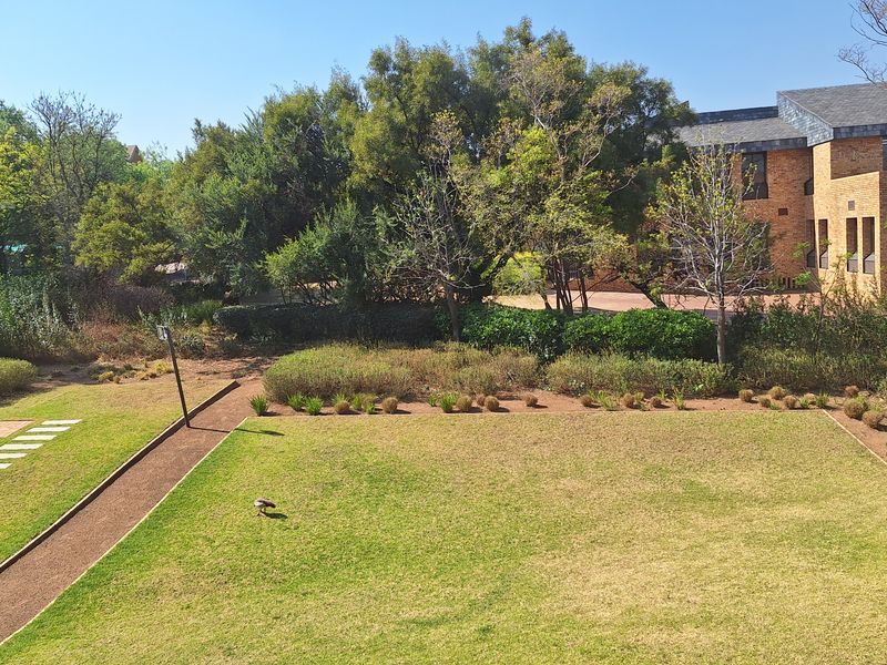 A well-maintained communal garden area featuring a large lawn, paved pathways, and mature landscaping adjacent to a brick office building.