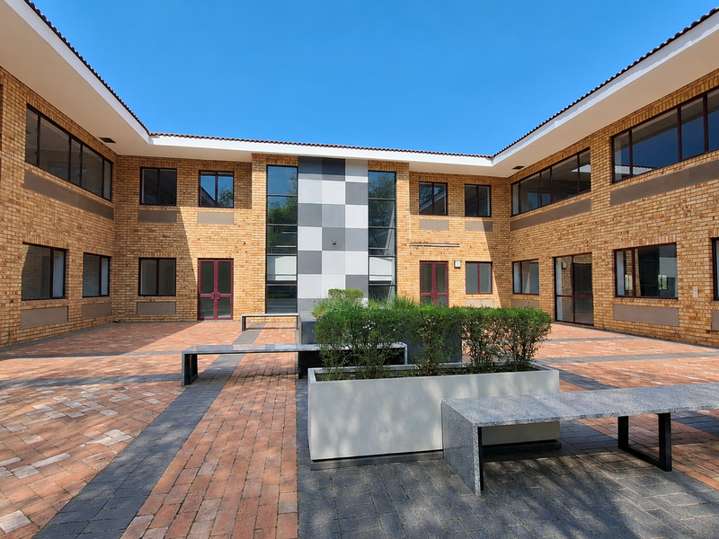 A well-maintained office courtyard featuring brick architecture, paved flooring, built-in stone seating, and integrated planters within a central open-air space.