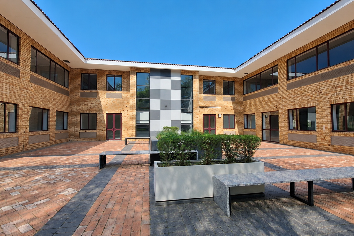 A well-maintained office courtyard featuring brick architecture, paved flooring, built-in stone seating, and integrated planters within a central open-air space.