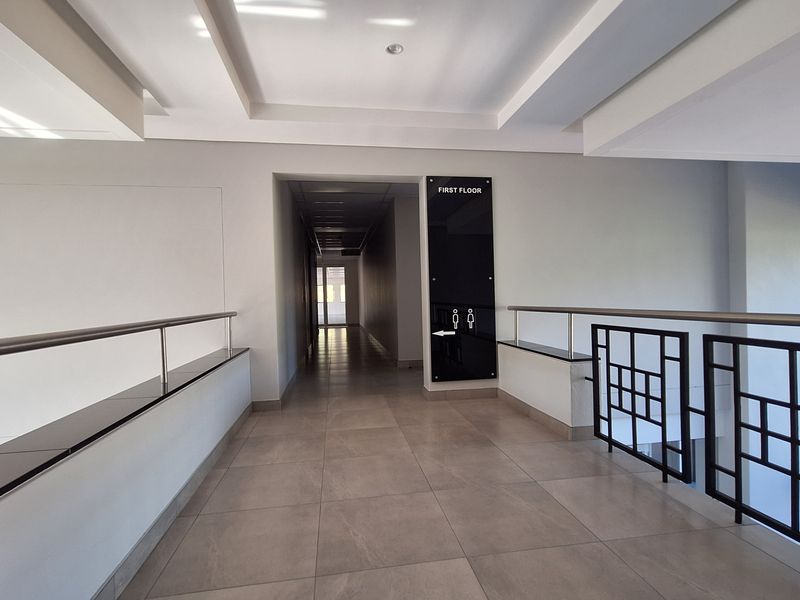 A clean, modern office hallway featuring tiled flooring, recessed ceiling details, and a metal balustrade overlooking the lower level.