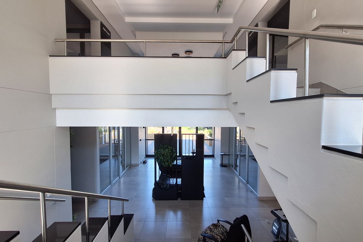 Spacious modern office entrance featuring a grand staircase, mezzanine level, and clean tiled flooring with glass partitioning throughout the open-plan layout.