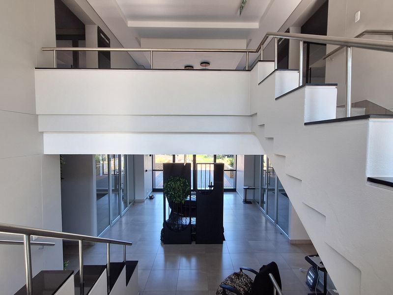 Spacious modern office entrance featuring a grand staircase, mezzanine level, and clean tiled flooring with glass partitioning throughout the open-plan layout.