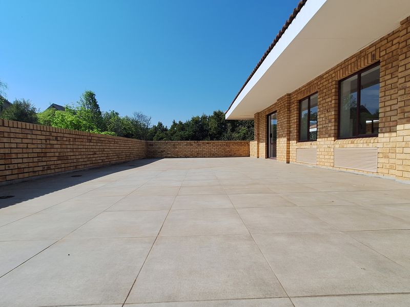 A spacious, well-maintained outdoor patio area featuring face brick walls, large windows, and clean tiled flooring under a wide overhanging roof.
